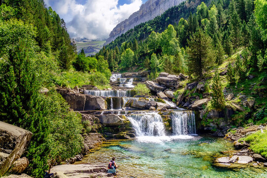 Waterfall on steps or terraces in green landscape between trees and mountains in Ordesa. Soaso stands.
