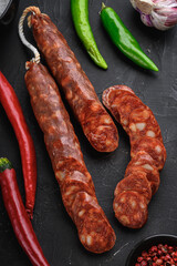 Spanish chorizo  sausage slices  with herbs and spices on black textured background, topview