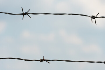 Two rows of barbed wire against a blue sky. Protection of life and property. Protection of criminals in prison. Peaceful sky overhead through the prism of violence and cruelty of modern times.