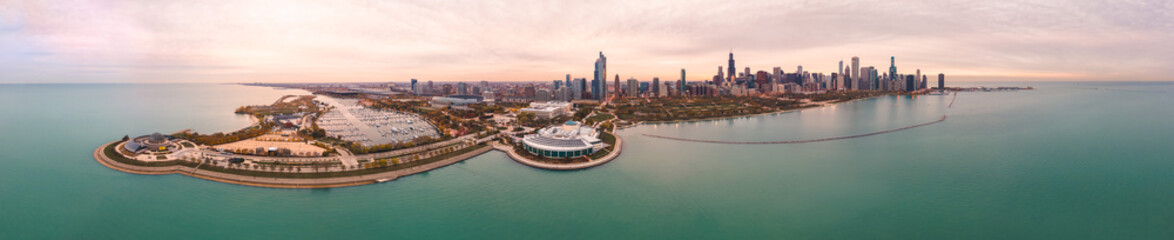 Obraz premium Incredible wide angle Chicago city skyline aerial panorama over Lake Michigan with highrise skyscraper buildings and boat harbors along the horizon with a beautiful orange and blue sunset sky above.