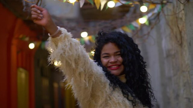 afro American young woman celebrating Christmas with sparklers outdoors in the street, dancing, enjoying winter holidays