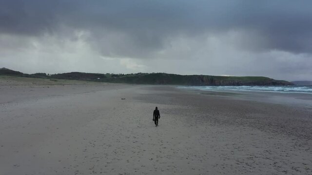 Back view of man walking alone on empty deserted beach on winter cloudy day