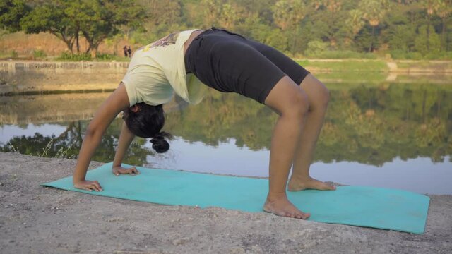 Indian girl doing upward bow weel pose urdhva dhanurasana yoga pose by the lakeside