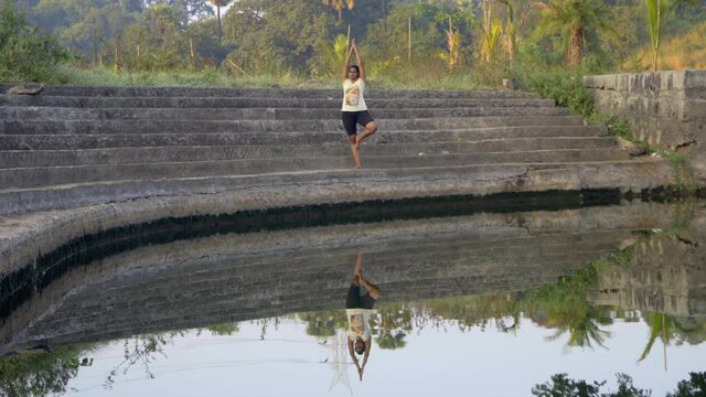 girl doing tree pose vrhsasana double image reflection  in still water on steps of lade