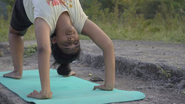Indian girl doing upward bow weel pose urdhva dhanurasana yoga pose by the lakeside face close front shot