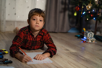 portrait of little boy laying on the floor in his room writing christmas letter to santa. Image with selective focus