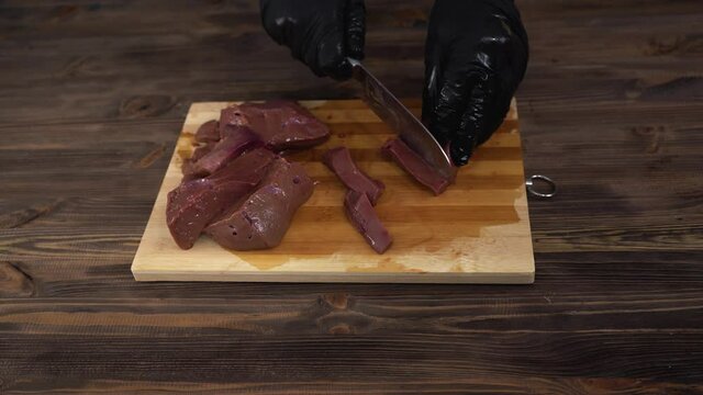 a chef in black gloves cuts beef liver into slices with a kitchen knife