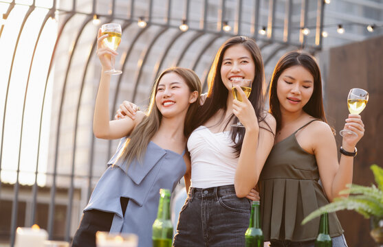 Happy Young Asian Women Gang Drinking Champagne While Enjoying Rooftop Bar Party. Girls Best Friends Having Fun At Terrace Party. Concept About Women Night Out.