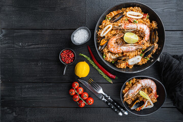 Valenciana seafood paella in bowl and frying pan on black wooden planks, top view with space for text