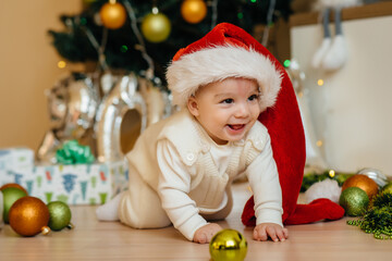 Cute smiling baby is lying under a festive Christmas tree and playing with gifts. Christmas and New Year celebrations