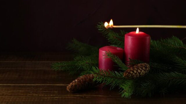 Christmas candles and lights. Two burning candles with fir branch and cones over wooden background, still life