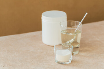Glass with collagen dissolved in water and collagen protein powder on a light beige table. Healthy lifestyle concept.