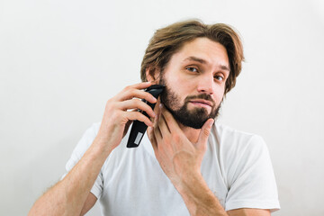 Handsome Bearded Man Trimming His Beard With a Trimmer at Morning in the Bath Room. Beauty, Hygiene, Shaving, Grooming and People Concept.