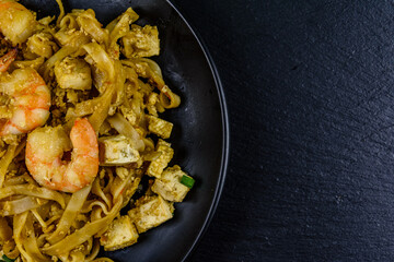 Black plate with pad thai on a slate board. Top view