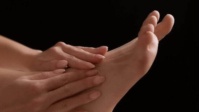 Unrecognizable young woman massaging her injured foot, pain and sprain in ankle. Close-up.