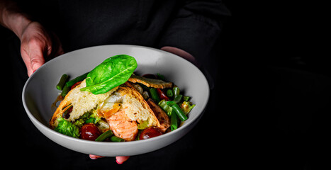 chef in a black suit holds in his hands bowl with salad on Dark grey black background