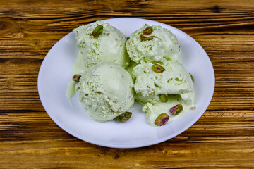Glass bowl with pistachio ice cream balls and nuts on a wooden table
