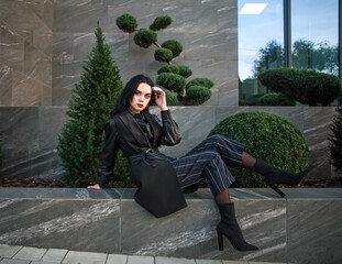 Young girl model in fashionable clothes on background of black stone wall and green plants,...