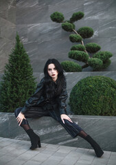 Young girl model in fashionable clothes on background of black stone wall and green plants,...
