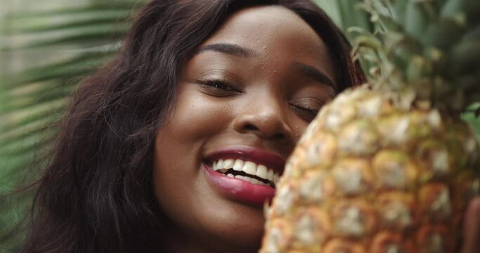 Young beautiful girl with natural makeup holds a pineapple in her hands and smiles at the camera. Against the background of tropical forest and wildlife. Shooting close up of emotion smile. The