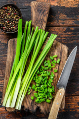 Cut Green onions chives on a cutting board. Dark wooden background. Top view - obrazy, fototapety, plakaty