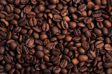 Scattered piles of roasted arabica coffee beans top view close up in daylight