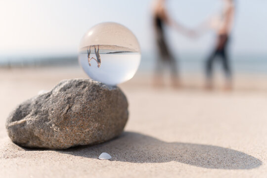 2 junge Mädchen Hand in Hand am Ostsee Strand , fotografiert durch eine Glaskugel
