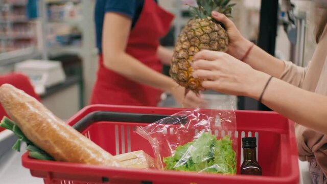 Midsection footage of unrecognizable female customer placing healthy products in red product basket after being scanned by cashier in hypermarket
