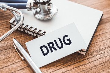 DRUG text on card on wooden table with stethoscope and notepad for medical records.