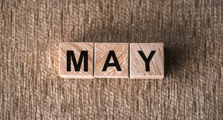 MAY is a word written on wooden cubes. On a brown background for your design, top view.