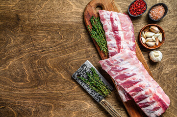 Raw pork rack spare ribs with spices, garlic cloves and thyme. Wooden background. Top view. Copy space