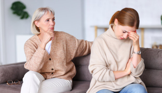 Upset women sitting on sofa after quarrel.