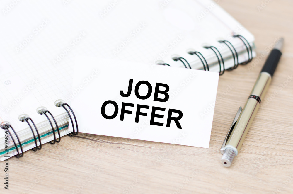Poster card with job offer text next to a notebook and a pen on a wooden table