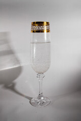 glass with golden ornament on white table casts shadow