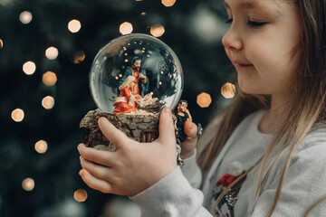 Girl looking at a glass ball with a scene of the birth of Jesus Christ in a glass ball