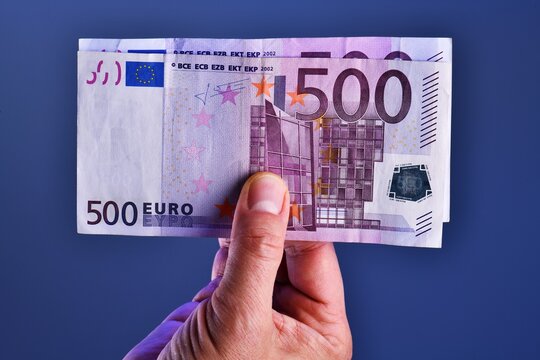 A man hand shows 1000 Euros in two 500 euro banknotes on a blue background