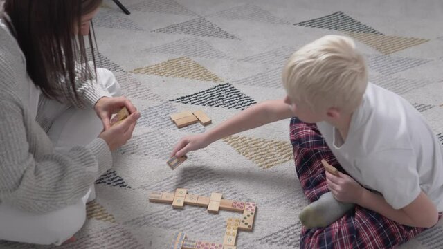 Mom and son play at home in wooden dominoes. Family intellectual games with children at home