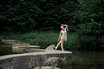 Fototapeta na wymiar A young blonde woman is dancing barefoot, with a winding concrete bridge behind her. Clothing of their eco-materials, macrame. The concept of natural products.