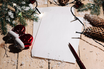 Christmas background from a table of snow-covered wooden boards, decorated with spruce legs, cones and a garland, and two white sheets of paper for congratulations. Christmas and New Year concept