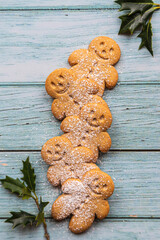 gingerbread cookies or gingerman arranged on a blue wooden table with holly, traditional Christmas plant - 397684898