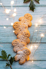 gingerbread cookies or gingerman arranged on a blue wooden table with holly, traditional Christmas plant, and Christmas lights - 397685071