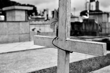 Black and white. Close-up of a cross surrounded by tombs in a cemetery.