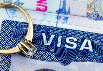 Engagement ring on top of blurred US entry visa sticker in a passport. Conceptual photo for fiance visa and immigration in general. Selective focus. - obrazy, fototapety, plakaty