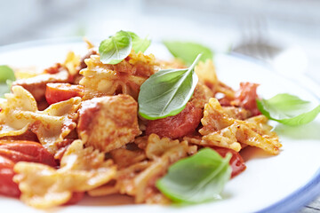 Farfalle pasta with chicken breast, cherry tomatoes and fresh basil. Bright wooden background. Close up.