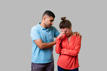 Obraz premium Portrait of unhappy worried young couple in casual wear standing together, man comforting crying woman, holding her shoulders, expressing sympathies. isolated on gray background, indoor studio shot