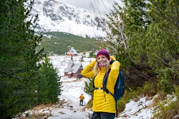 A happy blonde tourist in a yellow down jacket with a backpack spends his free time on mountain...