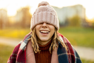 Cheerful woman covering eyes with knit hat while standing outdoors

