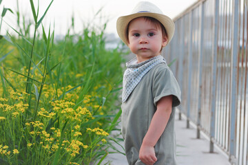 Stylish, happy child walks in the summer park by the river in a straw hat