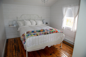 A white country cottage bedroom with an iron decorative bed, white lace curtains and a white...