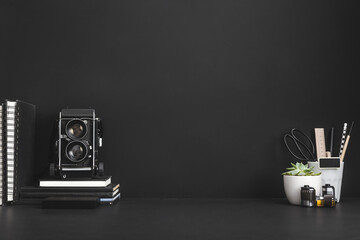 Home office desk with supplies, medium format camera and black wall background.